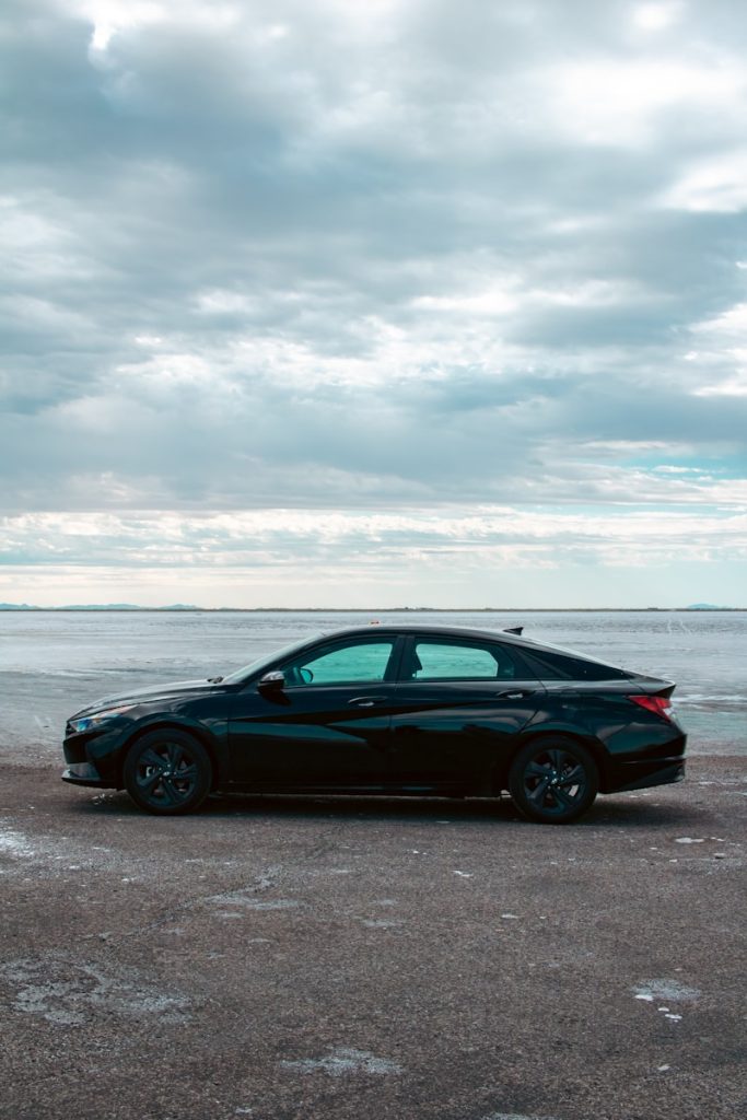 A black car parked on a beach next to the ocean